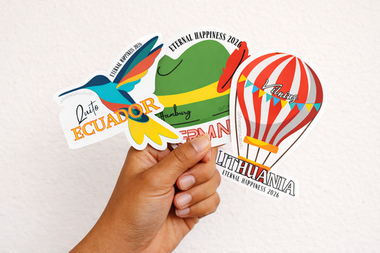 Hand holding a collection of international convention stickers with various designs on a white background
