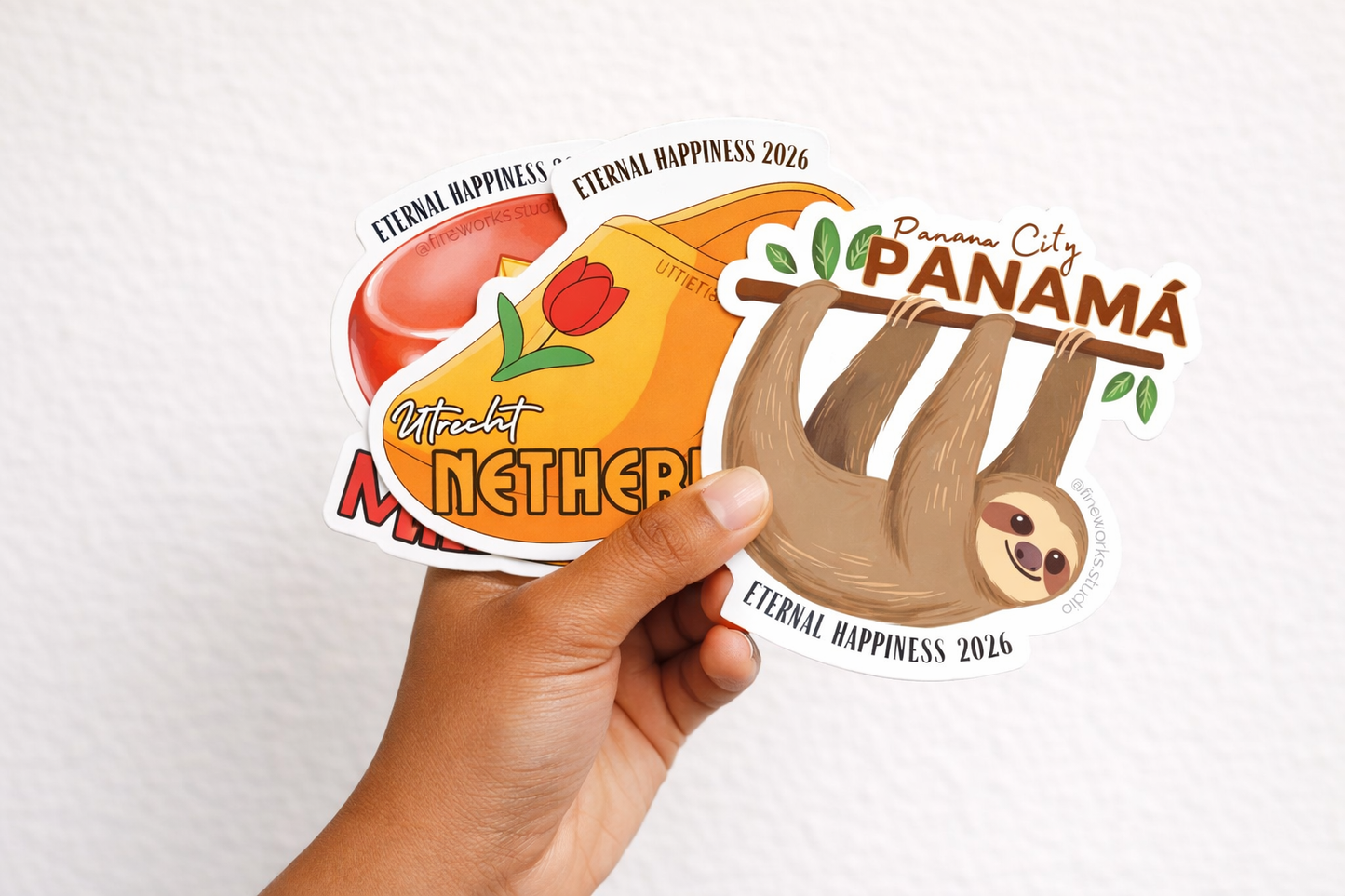 Hand holding a collection of international convention stickers with various designs on a white background